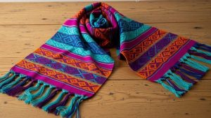 Traditional Mexican rebozo shawl with vibrant geometric patterns and hand-knotted fringe displayed on wooden surface